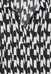 Musta ja valkoinen lyhythihainen paita, jossa on geometristen kuvioiden kaarevia muotoja, kaulus ja aavistuksen syvä kaula-aukko. Teksturoitu kangas.