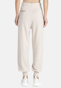 Jasno-beżowe dresy o luźnym kroju i zwężanych mankietach, z tylną kieszenią z kontrastowym wykończeniem oraz miękką teksturą.