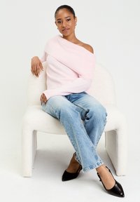 Pull léger rose, dénudé d'une épaule, avec texture côtelée, associé à un jean bleu clair à coupe décontractée et des escarpins noirs à bout pointu.