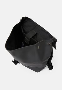 Svart vattentålig väska med en vikbar design, som har en vadderad insida och en justerbar rem. Inuti finns ett robust handtag för stöd.