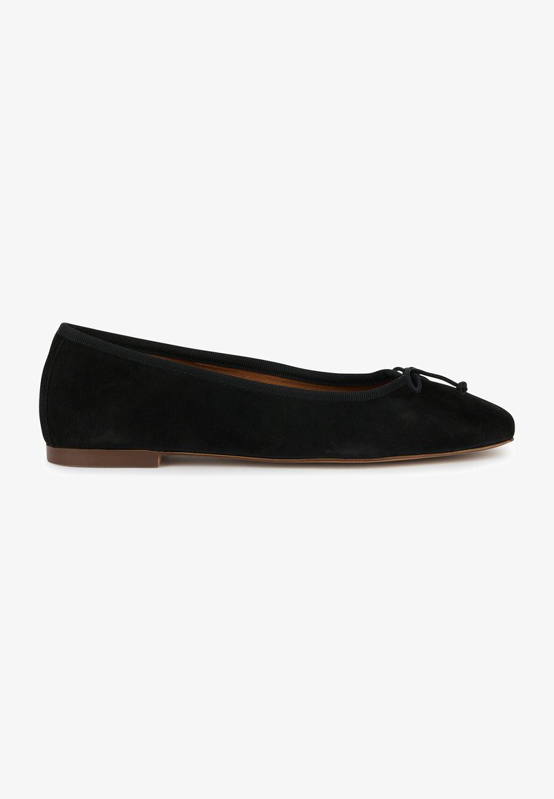 Ballerines en suede noires avec un bout pointu, semelle plate marron et un nœud en ruban noir à l'avant. Texture lisse et design minimal.