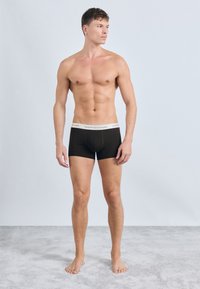 Crne bokserice s bijelim pojasom "TOMMY HILFIGER", koje se odlikuju uskim fitom, glatkom tkaninom i ravnim šavovima, prikazane na muškom modelu.