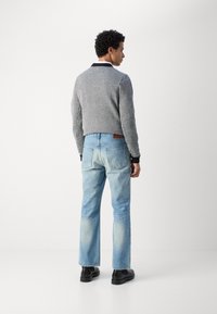 Grijze gebreide trui met zwarte kraag, gecombineerd met lichtblauwe denim jeans. Zwarte schoenen zichtbaar. Gezien vanuit de achterkant.