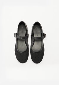 Black Mary Jane shoes with a smooth leather strap and a dotted texture on the upper. Rounded toe and flat sole.