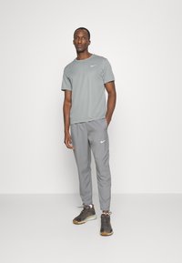 Grå Nike t-shirt og matchende bukser, begge med en glat tekstur. Skoene har en mørkegrå overdelle, lys sål og flerfarvede accenter.