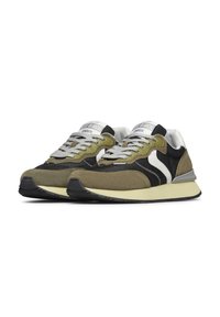 Un paio di sneaker in suede verde oliva e nero con accenti bianchi, lacci grigi e suole color crema, rivolti leggermente a sinistra su uno sfondo bianco.
