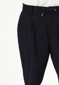 Pantaloni navy a coste con una finitura testurizzata, dotati di cintura con cordino e tasche laterali, mostrati dalla vita in giù.