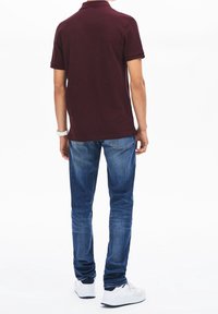 Polo bordeaux avec col, associé à un jean en denim bleu et des baskets blanches. Vue de dos, mettant en valeur la coupe et la couleur du polo.