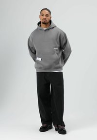 Grijze oversized hoodie met een voorzak, zwarte wijde broekspijpen en chunky zwarte schoenen met roze veters. Eenvoudig ontwerp, casual uitstraling.