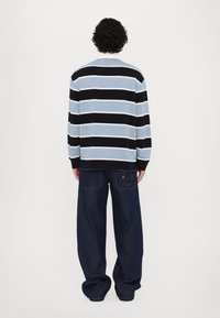 Langermet stripete skjorte i lys blå, svart og hvit, kombinert med mørkeblå vide jeans, sett bakfra.