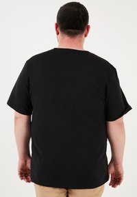 Černé tričko s krátkým rukávem a kulatým výstřihem, vyrobené z bavlny. Materiál má hladkou strukturu, uvolněný střih a není na něm žádný viditelný vzor.