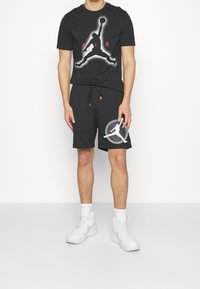 T-shirt noir avec un motif de basketball et le texte « AIR », assorti à un short noir avec un logo Jumpman. Porté avec des baskets blanches.