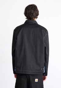 Sort jakke med skræddersyet pasform, med blå syningsdetaljer, en spredt krave og trykknapsdetaljer ved manchetterne og kanten.