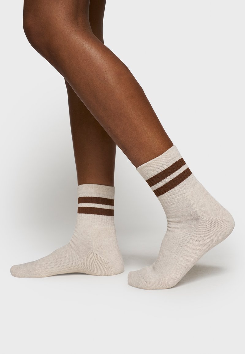 Beige Socken mit dunkelbraunen und weißen horizontalen Streifen, geripptem Textur und einem regulären Crew-Längen-Design, das ein glattes, weiches Material zeigt.