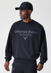 Černá mikina s nápisem "CHICAGO BULLS", logem a detaily sportovního sdružení. Dlouhé rukávy s žebrovanými manžetami a pasem.