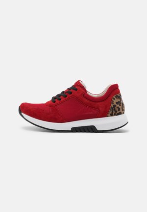 Rød sneaker med sorte snørebånd, hvid sål og leopardmønstret hældetalje på en lys grå baggrund, sidevisning.
