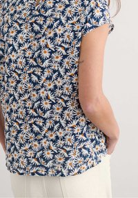 Floral blouse featuring a navy background with white daisies and orange centers, short sleeves, and a relaxed fit. Soft fabric texture.