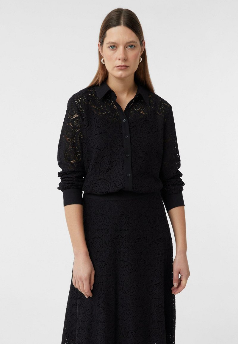 Black lace dress with intricate floral patterns, featuring a button-up collar, long sleeves, and a cinched waist design. Smooth texture.