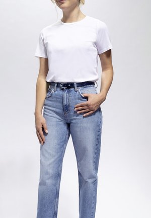 T-shirt bianca in cotone, maniche corte, abbinata a jeans in denim azzurro chiaro con vestibilità classica e una cintura scura. Tessuto liscio, senza motivi visibili.