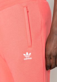 Rosa sweatpants i mjukt material med slim fit, som har en blixtlåsficka och en vit Adidas-logga på nedre benet.