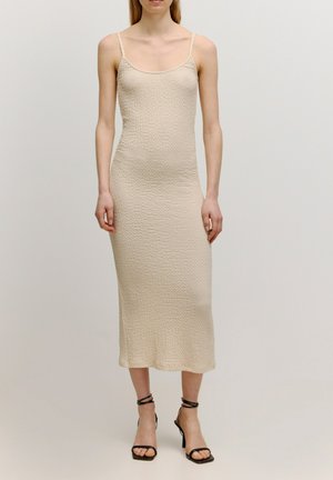 Beiges gestricktes Midikleid mit dünnen Trägern, strukturiertem Stoff, figurbetontem Design und geradem Saum. Kombiniert mit schwarzen, sandalen mit hohen Absätzen und Riemchen.