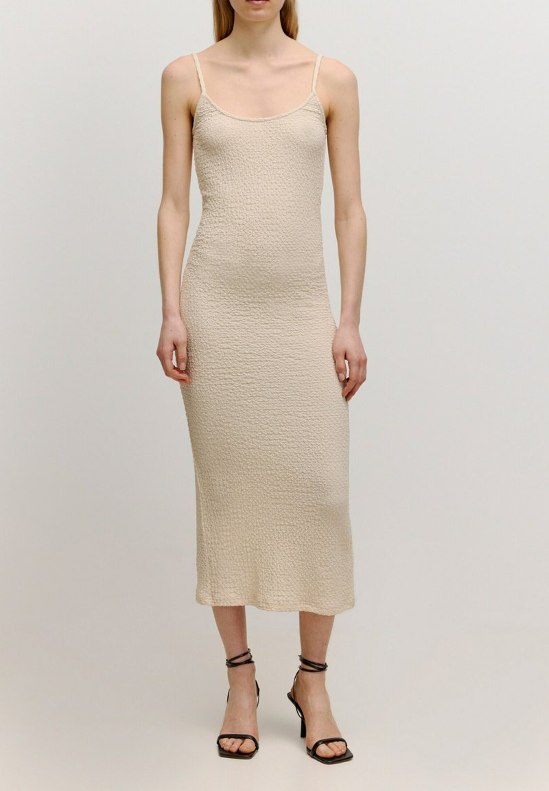 Beiges gestricktes Midikleid mit dünnen Trägern, strukturiertem Stoff, figurbetontem Design und geradem Saum. Kombiniert mit schwarzen, sandalen mit hohen Absätzen und Riemchen.