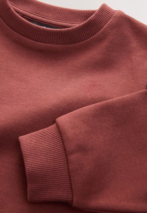 Sudadera con cuello redondo acanalado en color rosa polvoriento, con un material de algodón texturizado y puños acanalados para un ajuste ceñido. Superficie lisa con detalles mínimos.