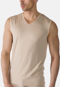 Top senza maniche beige a scollo a V realizzato in tessuto liscio. Presenta un design aderente e cuciture ridotte al minimo sul collo e sulle braccia.