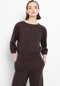 Pullover marrone a maglia con maniche a tre quarti, scollo ampio e orlo a coste, abbinato a pantaloni coordinati. Texture liscia.