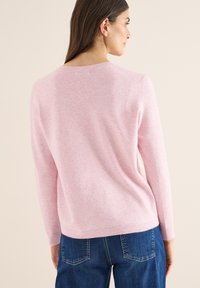 Suéter rosa claro hecho de material suave, con mangas largas, cuello redondo y corte holgado. Combinado con jeans de mezclilla azul.