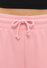 Gros plan sur un cordon de serrage rose noué à la taille d'un pantalon en tissu doux porté avec un haut court noir au-dessus.