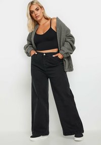 Mustat leveät farkut yhdistettynä mustaan crop-topiin ja tekstuuriltaan löysään harmaaseen neuletakkiin. Valkoiset tennarit täydentävät asun.