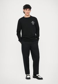 Czarna bluza z okrągłym dekoltem, z białym geometrycznym logo. Do tego czarne spodnie i czarno-białe buty.