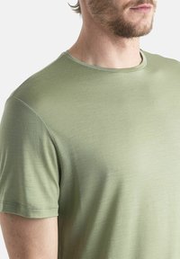 Olivově zelené tričko s krátkým rukávem, kulatý výstřih, hladká textura, lehký materiál, jemný lesk, čisté šití podél lemu a rukávů.