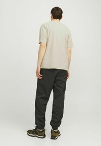Beige puuvillane T-särk, millele on sobitatud mustad elastsed püksid ja rohelise mustriga tossud; minimalistlik disain, lihtne lõige ja mugav istuvus.