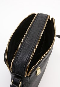 Schwarze Leder-Crossbody-Tasche mit strukturiertem Oberflächenmaterial, goldenen Reißverschlüssen und geräumigem Innenraum. Mit einem Logo-Tag und verstellbarem Tragegurt.