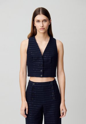 Gilet court bleu marine avec un col en V, ornée de rayures verticales argentées, deux poches avant et une fermeture à six boutons. Le matériau semble texturé.