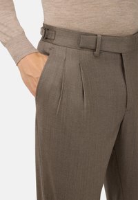 Pantaloni khaki con design su misura, pieghe e cintura con fibbia in metallo, realizzati in un tessuto testurizzato. Adatti per abbigliamento formale.
