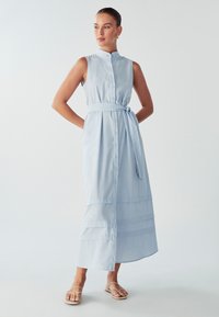 Šviesiai mėlyna, be rankovių, mygtukais užsegama suknelė su aukštu apykakle, juosmens diržu ir sluoksniuotu hemu. Lygus audinys, kasdienis dizainas.