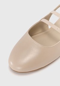 Ballerines beiges en cuir lisse avec un bout rond et des doubles brides. L'intérieur est légèrement rembourré pour plus de confort.