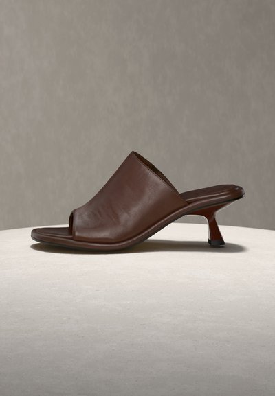 Brown leather open-toe mule shoe with a low, curved heel, displayed on a light surface against a neutral background.
