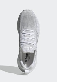 Fehér sportcipő, textúrált kötött felsőrésszel, fehér fűzőkkel és logó díszítéssel. Kerek talpa a kényelem érdekében.