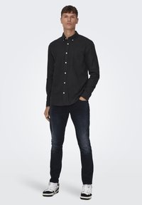 Zwarte button-up shirt met een borstzak, gedragen bij donkere jeans en zwart-witte sneakers. Slim fit en lange mouwen.