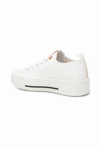 Zapatilla de lona blanca con un diseño de corte bajo, que presenta una suela texturizada, ojales naranjas y una franja negra en la entresuela.