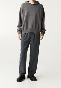 Szary, oversize bluza z kapturem, z prążkowanymi mankietami i dołem, zestawiona z ciemnymi, fakturowanymi spodniami z kordurowej tkaniny. Całość dopełniają czarne botki na masywnej podeszwie.