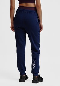 Marineblauwe sweatpants met een taps toelopende pasvorm, elastische tailleband en zilveren chevronaccenten op het linkerbeen. Gerecycled stof en boorden.