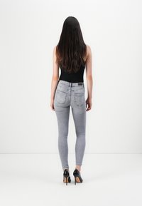 Sive uske traperice s stražnjim džepovima, uparene s crnim topom i crnim visokim potpeticama. Glatka denim tekstura, uski silueta.
