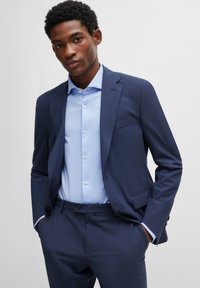 Marine pakjas met subtiele textuur, lichtblauw overhemd met knopen en bijpassende taillepantalon. Voorzien van een enkele borstzak en knopen.