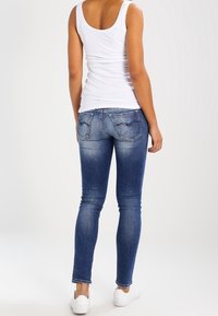 Smal blå jeans med en blekt tvätt, silverstygn och två bakfickor. Kombineras med en vit linne och vita sneakers.