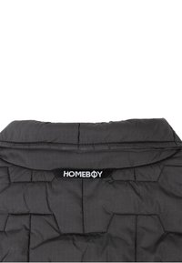 Črna podložena jakna z visokim ovratnikom, izraženim šivom in oznako, ki pravi "HOMEBOY" v kontrastni beli barvi.